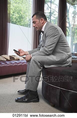 Stock Image - businessman sitting in bar checking his mobile phone for text messages. Fotosearch