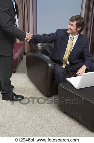 Stock Image - businessman sitting in leather chair shaking hands with friend. Fotosearch