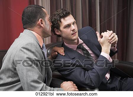 Stock Image - businessman whispering into his friends ear. Fotosearch