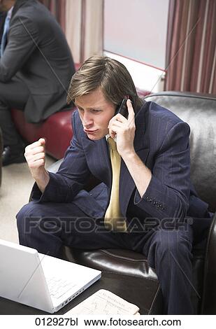 Stock Image - businessman with clenched fist sitting in front of notebook talking on his cellphone. Fotosearch