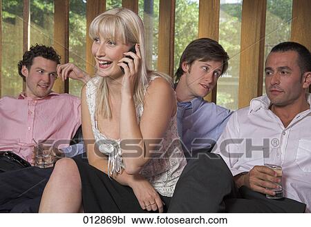 Stock Image - group of friends sitting together with woman having a conversation on her cellphone. Fotosearch