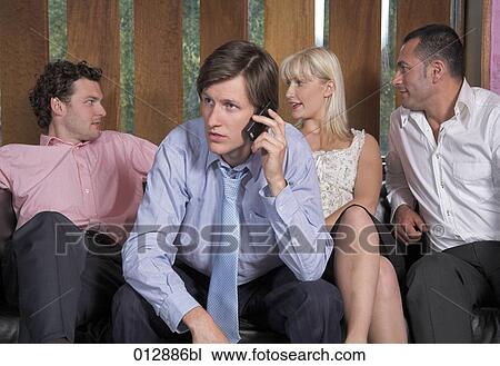 Stock Image - group of friends sitting together with man having a conversation on mobile phone. Fotosearch