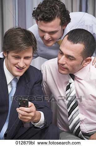 Stock Image - group of three businessmen looking interested at display of cell phone. Fotosearch