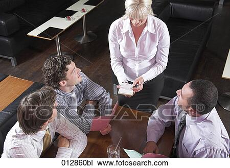 Stock Image - high angle view of waitress taking orders from three guests in restaurant. Fotosearch