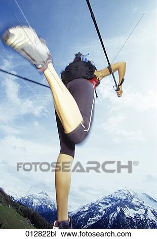 Stock Image - low angle view of woman doing nordic walking in mountain landscape. Fotosearch