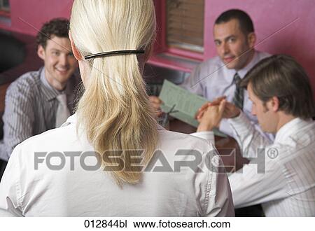 Stock Image - rear view of waitress taking orders from three men in restaurant. Fotosearch