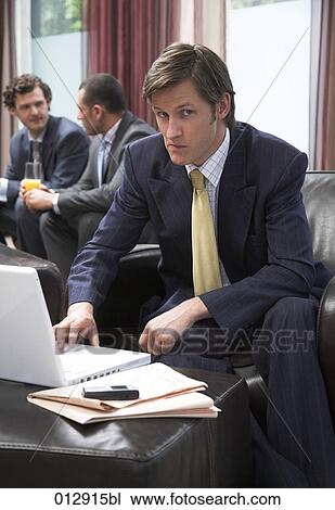 sceptical looking young businessman sitting in front of notebook computer View Large Photo Image Stock Image - sceptical looking young businessman sitting in front of notebook computer. Fotosearch