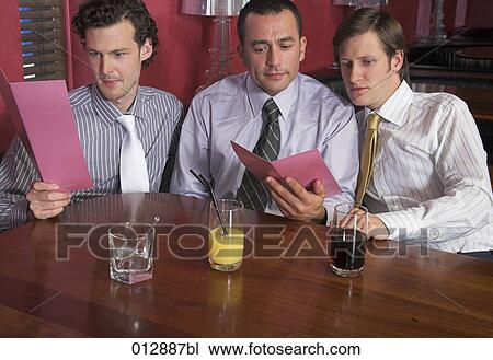 Stock Image - three male friends studying menu in restaurant together. Fotosearch
