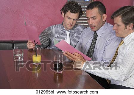 Stock Image - three men sitting in restaurant reading menu together. Fotosearch