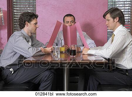Stock Image - three men studying menu in restaurant. Fotosearch