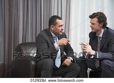 Stock Image - two businessmen enjoying a break smoking cigars and talking. Fotosearch