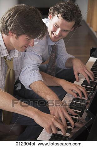 Stock Image - two good friends playing four handed piano. Fotosearch