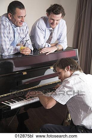 Stock Image - two men looking while their friend is playing piano. Fotosearch