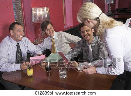 Stock Image - waitress taking orders from three male friends sitting in restaurant. Fotosearch