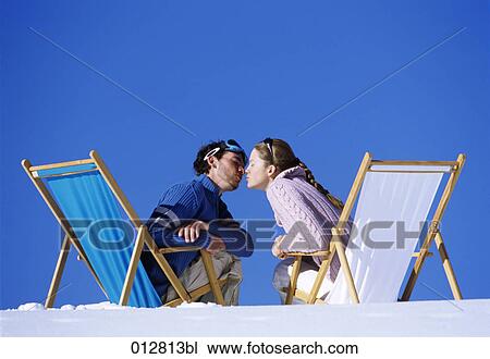 Stock Image - young couple sitting in deck chairs and kissing on mountain top. Fotosearch