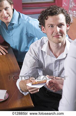 Stock Image - young man handing over credit card to pay in restaurant. Fotosearch