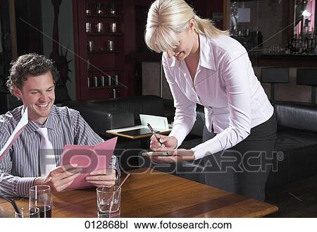 Stock Image - young waitress writing down order from guest in restaurant. Fotosearch