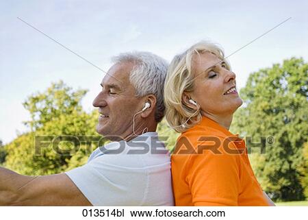 Stock Image - close-up of mature man and woman back to back listening to music. Fotosearch