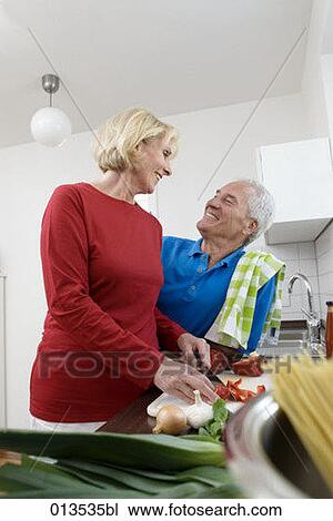 Stock Image - content mature couple looking at each other while preparing meal. Fotosearch