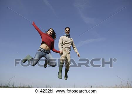 Stock Image - couple holding hands and jumping for joy. Fotosearch