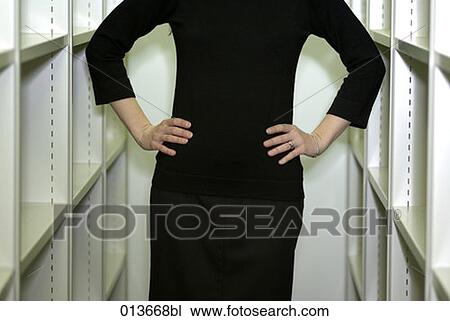 Stock Image - detail of woman standing between bookshelves. Fotosearch