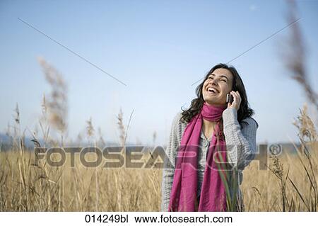 Stock Image - happy woman in field of reeds talking on cellphone. Fotosearch