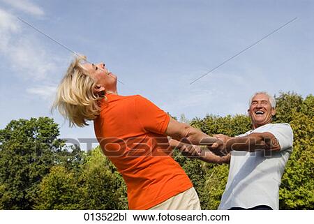 Stock Image - mature couple joyfully dancing in park. Fotosearch