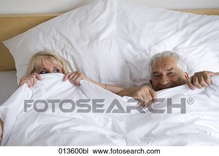 Stock Image - mature couple playfully hiding under blanket. Fotosearch