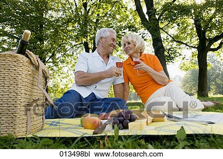 Stock Image - mature couple raising their glasses having picnic in park. Fotosearch