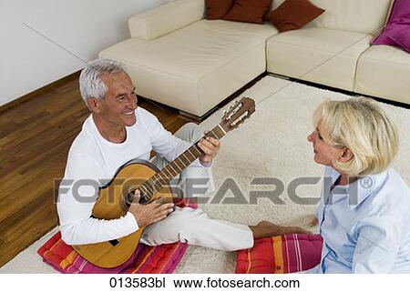 Stock Image - mature couple sitting floor in living room man playing guitar. Fotosearch