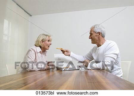 Stock Image - mature man playfully feeding wife with pizza. Fotosearch