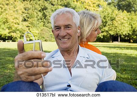 Stock Image - mature man sitting with his wife in park listening to music. Fotosearch