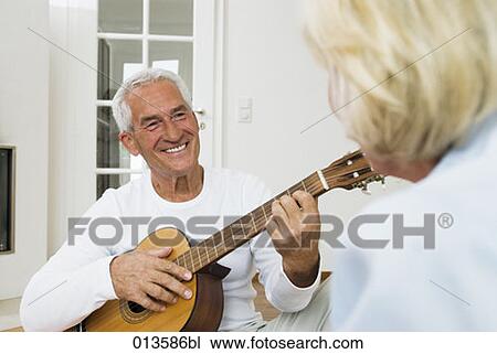 Stock Image - mature man smiling at his wife while playing guitar. Fotosearch