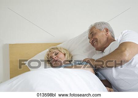 Stock Image - mature man waking up his sleeping wife. Fotosearch