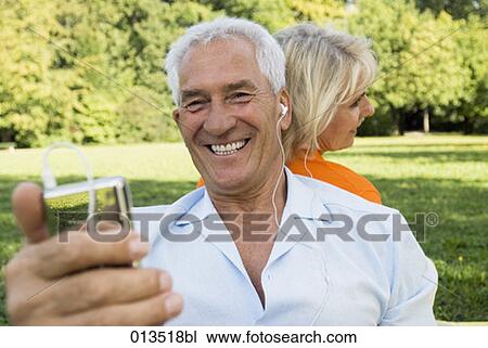 Stock Image - mature man with broad smile listening to music from mp3 player. Fotosearch