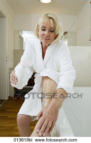 Stock Image - mature woman in bathrobe putting lotion on foot. Fotosearch