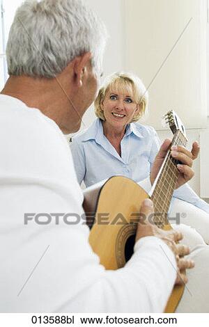 Stock Image - mature woman looking at her husband playing guitar. Fotosearch