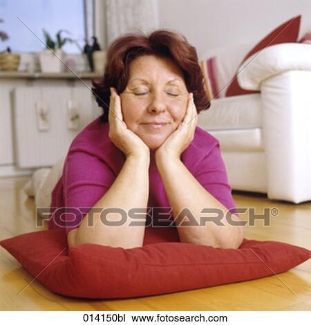 Stock Image - mature woman lying on floor day-dreaming. Fotosearch