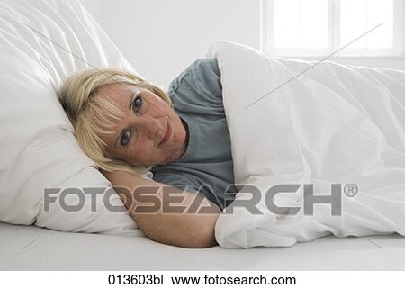 Stock Image - portrait of mature woman lying in bed. Fotosearch