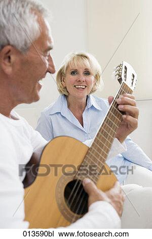 Stock Image - portrait of smiling mature woman looking at her husband playing music with guitar. Fotosearch