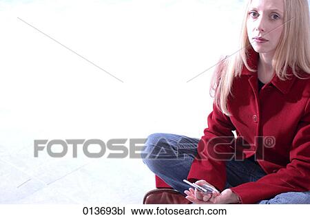 Stock Image - portrait of young woman sitting cross-legged with mobile looking serious. Fotosearch