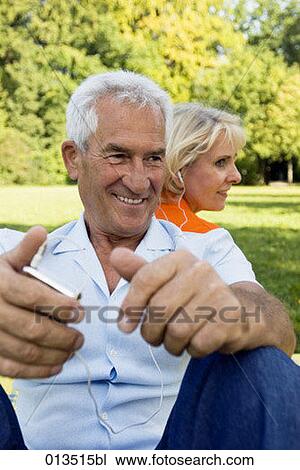 Stock Image - smiling mature couple sitting back to back man holding mp3 player. Fotosearch
