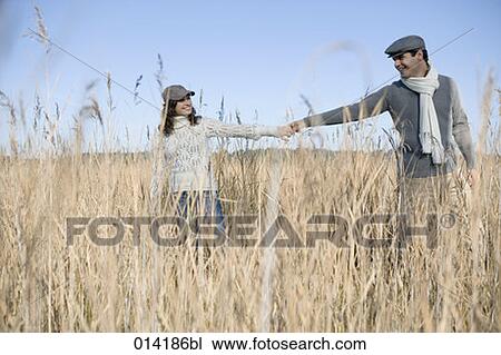 Stock Image - young couple smiling at each other and holding hands in field. Fotosearch