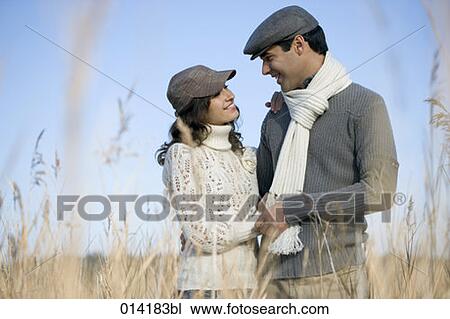 Stock Image - young couple smiling at each other in autumnal field. Fotosearch
