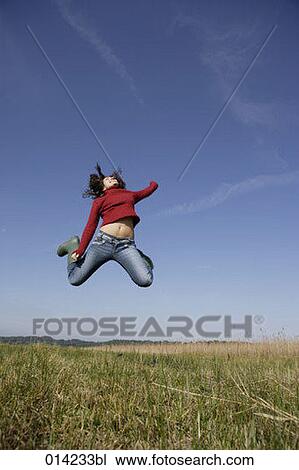 Stock Image - young woman doing high jump in field. Fotosearch