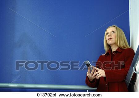 Stock Image - young woman looking up while texting on her cellphone. Fotosearch