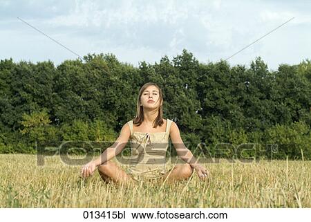 Stock Image - young woman sitting in field meditating. Fotosearch