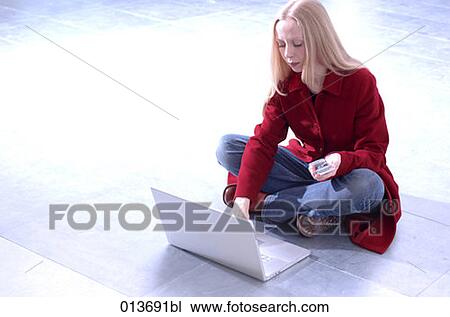 Stock Image - young woman working with laptop and holding cellphone. Fotosearch