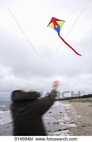Stock Image - blurred image of man playing with kite on beach in autumn. Fotosearch