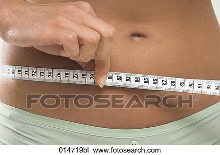 Stock Image - close-up of young women controlling her waistline with tape measure. Fotosearch